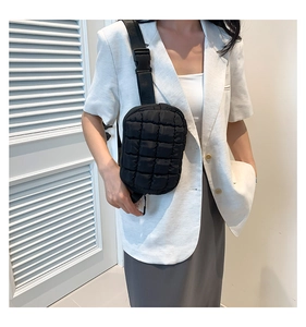 Close-up of black quilted crossbody bag on white blazer model with wide strap and buckle