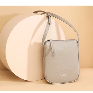 Minimalist beige pebble leather crossbody bag with top zipper and adjustable shoulder strap