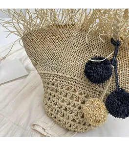 Dettaglio borsa in paglia intrecciata con frange in rafia e ciondoli pompon colorati