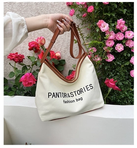 Close-up of canvas tote bag with brown leather trim held against a floral background
