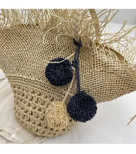Dettaglio di borsa in paglia intrecciata con sfere decorative in rafia e frange