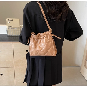 Detail view of brown quilted PU leather crossbody bag with drawstring on female model