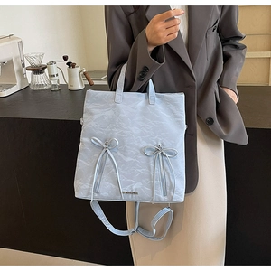 Detail of light blue pleated PU leather tote bag worn by a model in a cozy cafe setting