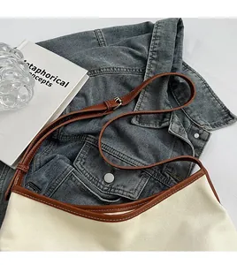 Detail of canvas shoulder bag with brown leather trim and adjustable metal buckle