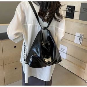 Detail of high-gloss black PU leather shoulder bag with silver butterfly metal ornament