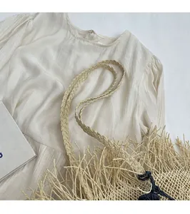 Dettaglio borsa di paglia intrecciata con frange e tracolla intrecciata su fondo lino