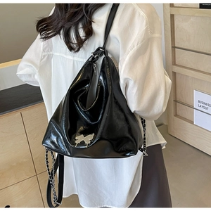 Detail of black patent leather backpack featuring silver butterfly metal ornament and strap