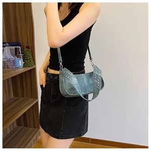 Detail of washed blue denim shoulder bag with silver punk studs on a female model