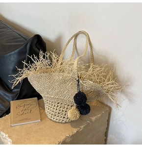 Dettaglio della borsa in paglia intrecciata con bordi sfrangiati e pompon decorativi