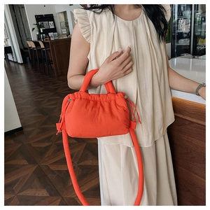 Detail of a bright orange puffer mini crossbody bag showing soft quilted texture and handles