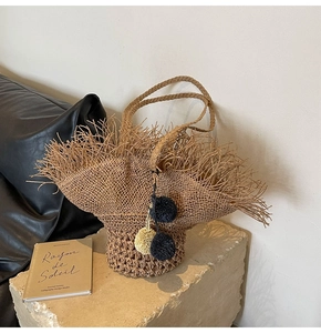Dettaglio della borsa tote in paglia intrecciata con pompon decorativi e bordi sfrangiati