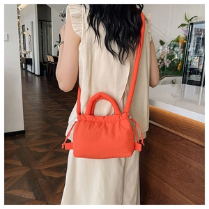 Quilted bright orange nylon crossbody bag shown worn by a model in a cozy cafe setting