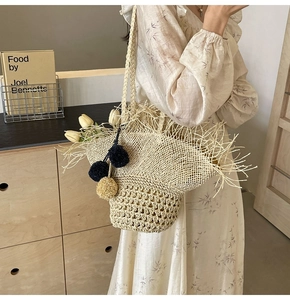 Dettaglio della borsa in paglia intrecciata con pompon decorativi e frange in paglia