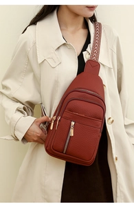 Detail of red-brown pebble leather chest bag with patterned strap on a beige trench coat