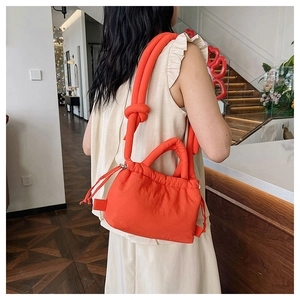 Detail of bright orange quilted crossbody bag with drawstring closure and knotted strap