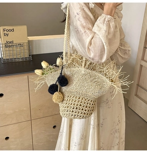 Dettaglio della borsa in paglia intrecciata con bordi sfrangiati e ciondoli a pompon colorati