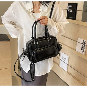 Detail of a black shiny PU leather Boston handbag with a front zipper pocket and adjustable strap