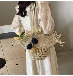 Dettaglio della borsa in paglia bohémien con lunghe frange e ciondoli pompon colorati