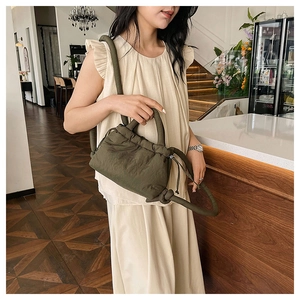 Detail of dark green pleated drawstring crossbody bag with textured fabric and knotted handle