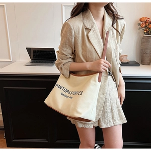 Detail of cream canvas crossbody bag with brown leather trim and fashion text print