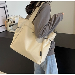 Detailed side view of beige canvas tote bag with drawstring and black brand tag