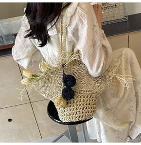Dettaglio della borsa tote in paglia intrecciata a mano con pompon e frange
