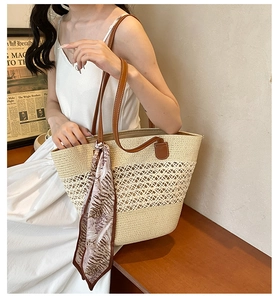 Detailed close-up of a woven straw tote bag with brown leather handles and leaf print scarf
