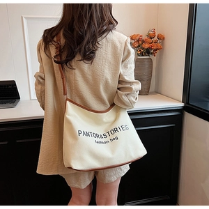 Detail view of cream canvas crossbody bag with brown leather trim worn by model in home setting