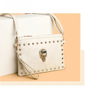 Close-up of white crossbody bag with gold skull crystal and metal rivet accents
