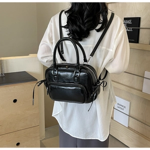 Rear view of model wearing a black PU leather backpack with silver metal zippers