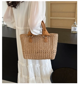 Close-up of woven straw handbag with knotted brown leather handle and gold hardware