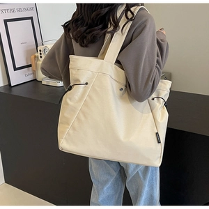Detail shot of a minimalist cream canvas tote bag with black drawstring and woven label