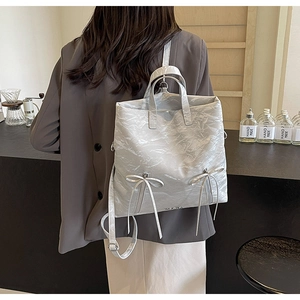 Detail of silver pleated PU leather backpack with bow knots and metallic zippers
