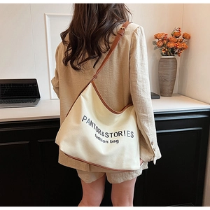 Detail of cream canvas tote bag with brown leather trim and adjustable shoulder strap