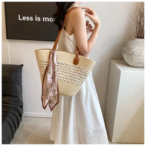 Close-up of straw tote bag with cutout weave, leather handles, and floral silk scarf detail