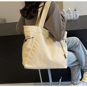 Detail of canvas tote bag showing side drawstring design and black woven brand label
