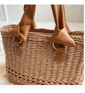 Close-up of woven straw handbag featuring a knotted leather handle and gold metal ring details