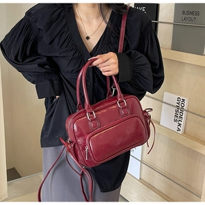 Detail of burgundy glossy oil wax leather handbag with smooth metallic zipper and crossbody strap