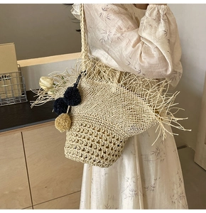 Dettaglio borsa in paglia intrecciata a mano con frange bohémien e ciondolo a pompon