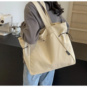 Detail of beige canvas tote bag with adjustable side drawstring and woven brand label