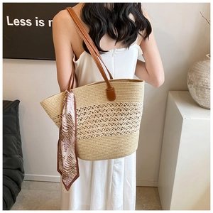 Close-up of beige woven straw tote bag with brown leather straps and a decorative silk scarf