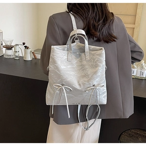 Detail view of the pleated PU leather texture with bow ribbons on the light gray backpack