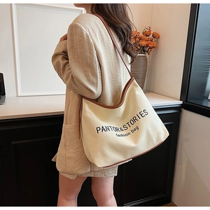 Detail of canvas tote bag with brown leather straps shown on a model in a minimalist room