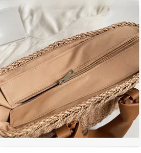 Close-up of metal zipper closure and brown leather handle on woven straw handbag