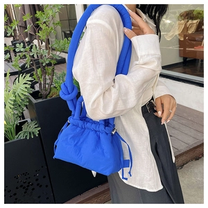 Detail of bright blue puffed crossbody bag with drawstring closure and knotted wide strap