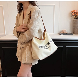 Detail of minimalist cream canvas crossbody bag with brown leather trim and text