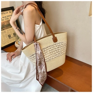 Detail of hand-woven straw tote bag with brown leather straps and floral decorative scarf