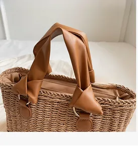 Detailed view of woven straw bag with brown leather handles and golden metal ring