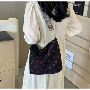 Detail of black corduroy hobo bag with strawberry print and bohemian shoulder strap