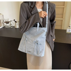 Close-up of light blue PU leather handbag with elegant bow details and metallic brand logo